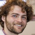 Gabriel Cohn, Ph.D. (Courtesy) Gabriel has full brown curly hair and is wearing a lab coat while pipetting in the lab.